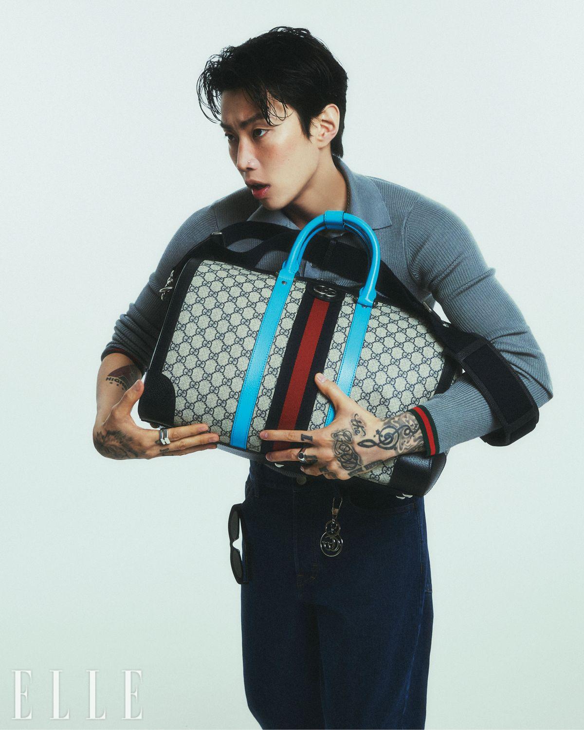 형광 블루 컬러가 포인트인 GG 모티프와 웹 스트라이프 디자인의 구찌 사보이 더플백, 니트 톱, 데님 팬츠, 검지에 착용한 트레이드마크 디테일의 스털링 실버 링, 중지에 착용한 트레이드마크 신 링, 더블 G 키 링, 선글라스는 모두 Gucci.