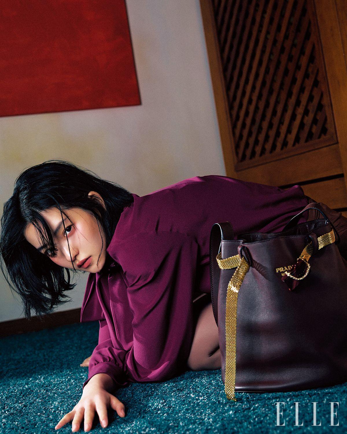 리본 디테일의 실크 블라우스와 스커트, 버클 레더 버킷 백은 모두 Prada. 