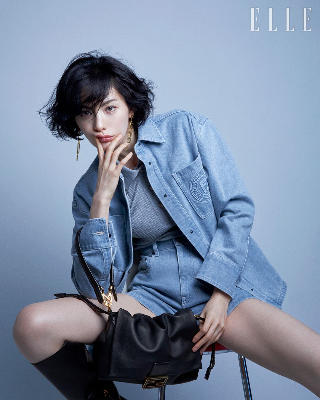 끈을 조이는 방식의 스트링 여밈이 특징인 펜디 맘마 백. 부드러운 나파 가죽 소재의 펜디 스몰 맘마 백, 싱글브레스트 셔츠 칼라의 라이트 블루데님 재킷과 쇼츠, 하이힐 부츠, 펜디 레터링 드롭 이어링은 모두 Fendi.