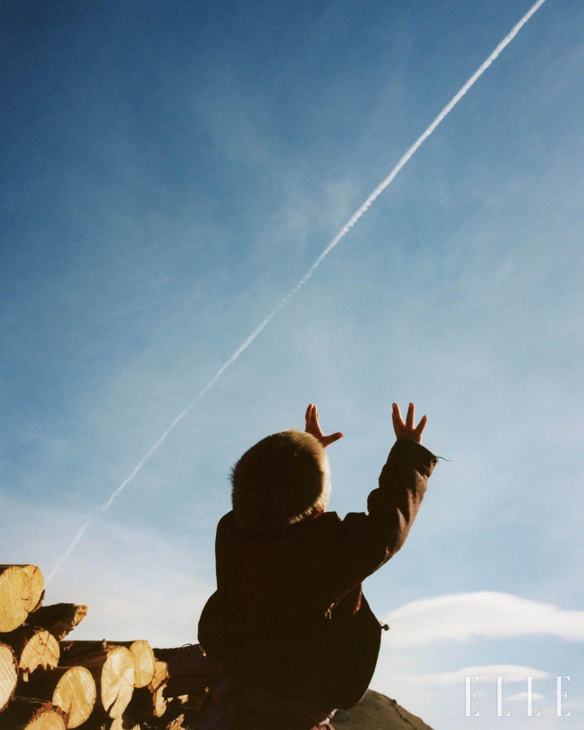 나무장작을 가지고 게르로 돌아오는 길, 하늘로 지나간 비행기 자리에 남은 구름을 잡으려 손을 뻗는 아욘볼드(Oyunbold). 