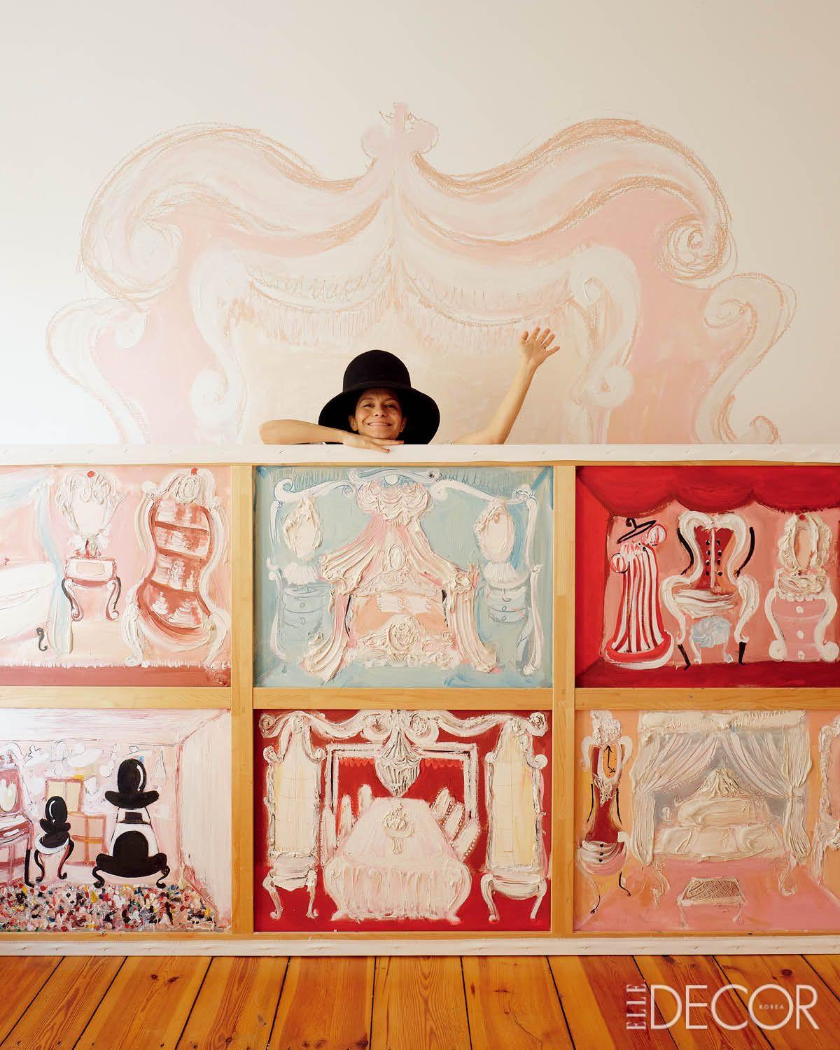 벽화 앞으로 여러 개의 회화 작품을 이어 붙인 패널을 들고 있는 메리엄. 그림 속의 초현실 세계와 실제 공간이 부드럽게 맞닿는다.