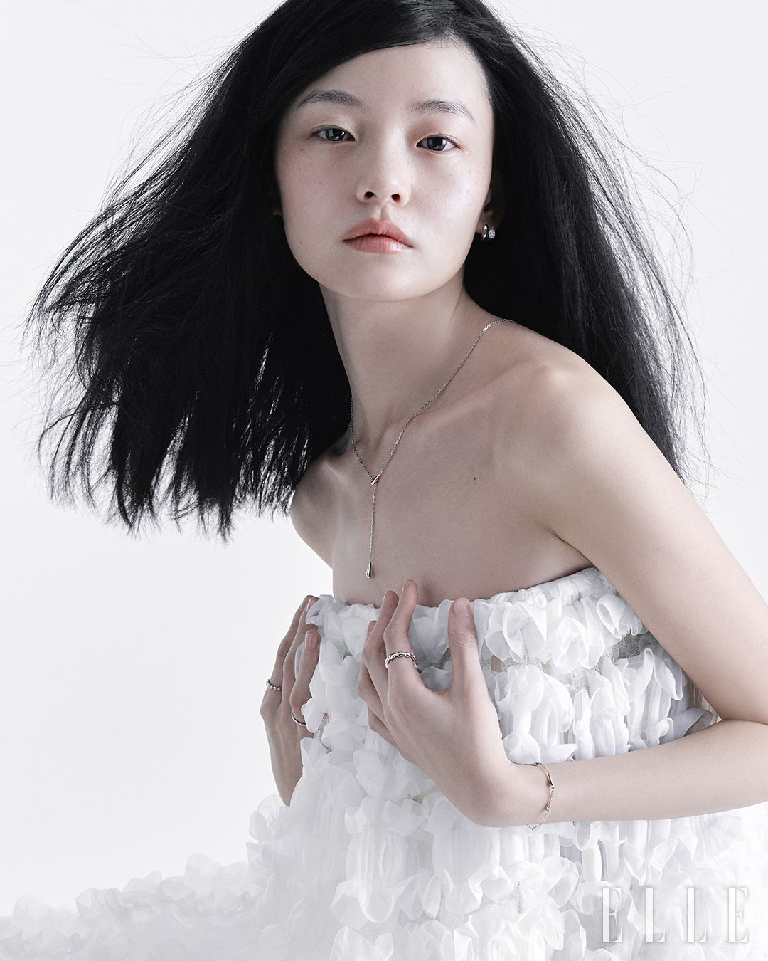 실버 소재의 듀엘 이어링, 듀엘 네크리스, 오른손 검지에 착용한 실버 소재의 듀엘 링, 약지에 착용한 14K 화이트 골드 소재의 벨라 링, 왼손에 착용한 실버 소재의 듀엘 링, 듀엘 브레이슬릿은 모두 STONEHENgE.