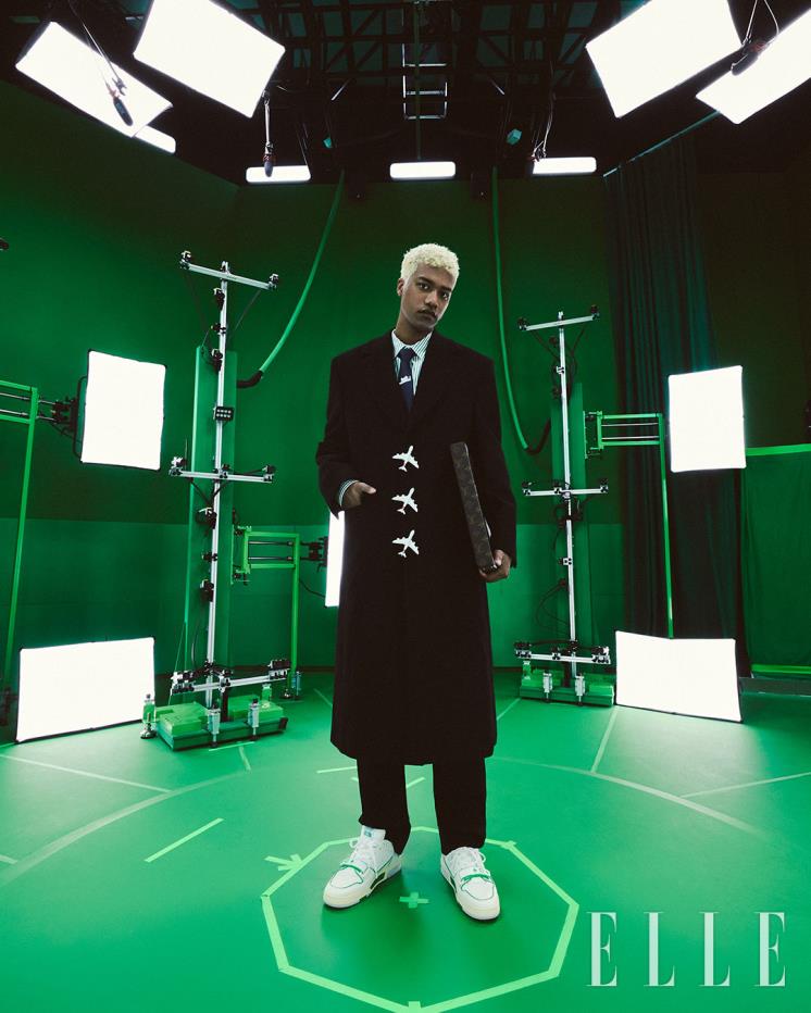 비행기 펜던트 버튼으로 포인트를 준 블랙 롱 코트와 스트라이프 셔츠, 팬츠, 모노그램 패턴의 피자박스, 청키한 스니커즈, 타이는 모두 Louis Vuitton. 