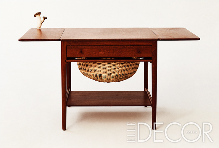 확장 가능한 양 날개, 라탄 바스켓이 특징인 티크와 오크 소재의 소잉 테이블은 Hans Wegner by Le Pavillon.