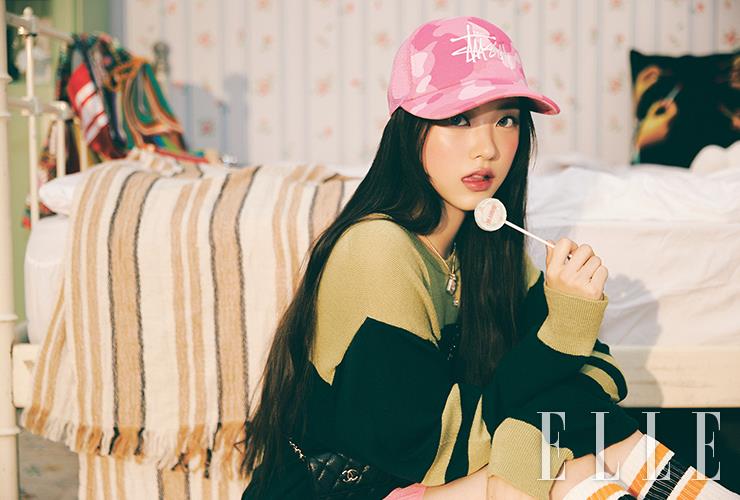 해린의 보송한 양볼에 N°1 DE CHANEL 레드 까멜리아 립 앤 치크 밤, 5 라이블리 로즈우드를 발라 핑크빛 생기를 더한다. 입술에 루쥬 알뤼르 렉스트레, 868호를 가볍게 두드려 발라 버건디빛이 가미된 레드 립을 표현. 사용 제품은 모두 Chanel. 미니 체인 백과 네크리스는 모두 Chanel. 니트 톱과 쇼츠, 모자와 니 삭스는 모두 스타일리스트 소장품.