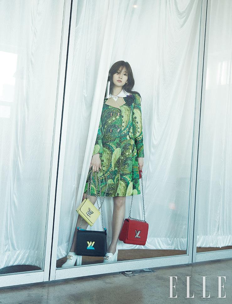 현란한 프린트의 미니 트렌치코트와 윙 칼라 화이트 셔츠, V 모티프 이어링, 옐로·레드·블랙 컬러의 트위스트 백, 화이트 부티는 모두 Louis Vuitton.