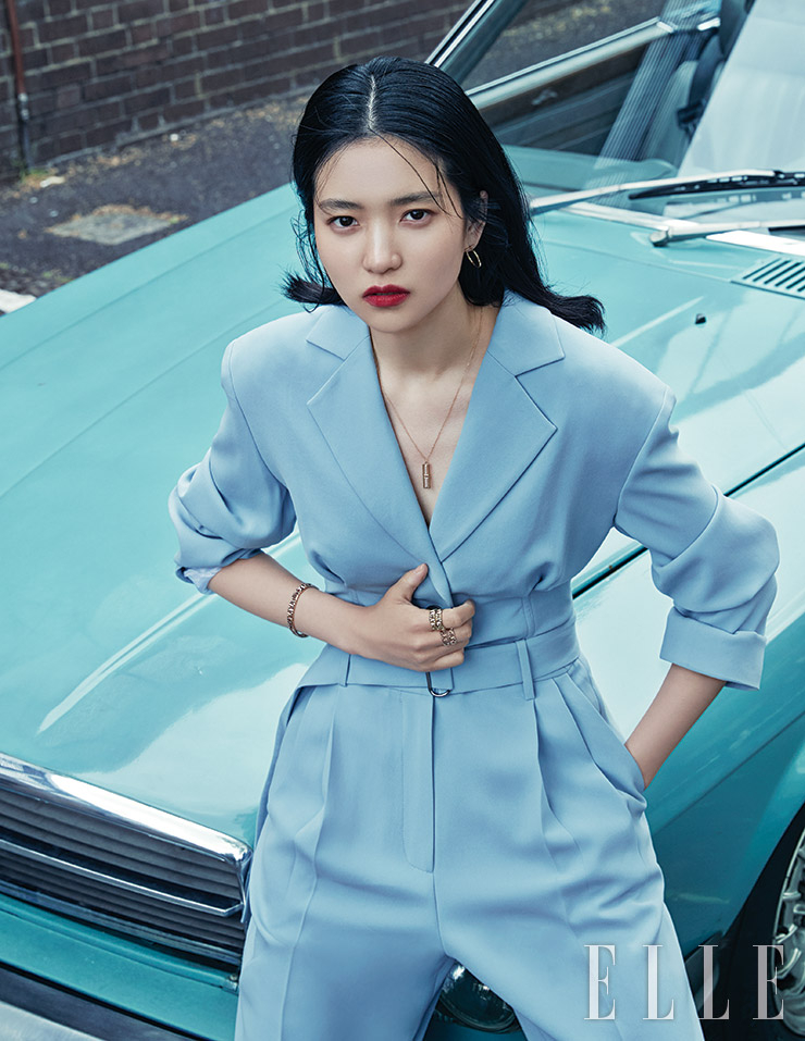 옐로골드 티파니 T 와이어 후프 이어링, 세련된 디자인의 티파니 T 투 오픈 버티컬 바 펜던트, 레이어드한 티파니 T 트루 와이드 링, 티파니 T 트루 내로 브레이슬렛 링은 모두 Tiffany & Co. 재킷과 트라우저는 모두 Moon Choi.