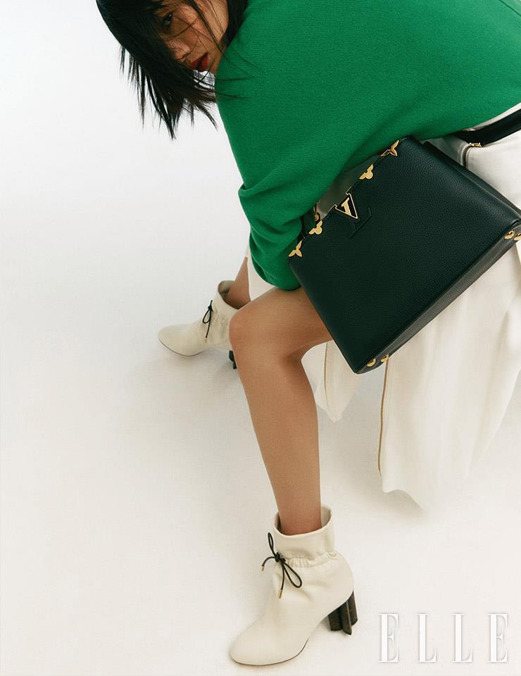 메탈 소재의 모노그램 플라워 장식을 더한 ‘카퓌신MM’ 백, 니트 스웨터와 플리츠스커트, 앵클부츠는 모두 Louis Vuitton.