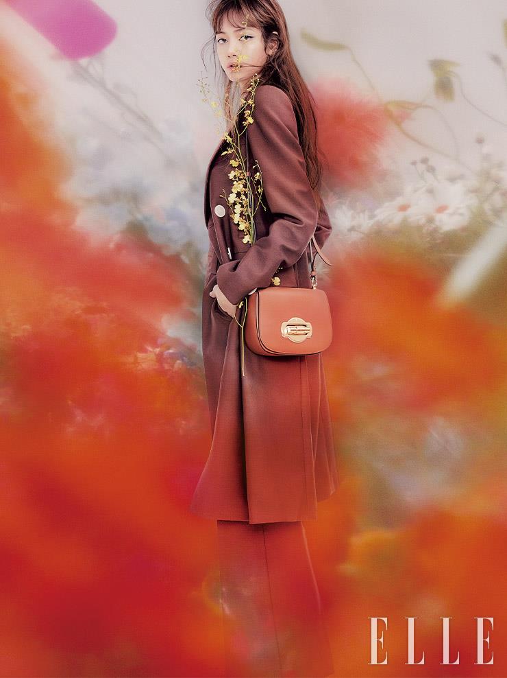 브라운 컬러 스프링 맥시 코트와 팬츠, 골드 버클 장식 트위스트 클로저 숄더백은 모두 Prada.