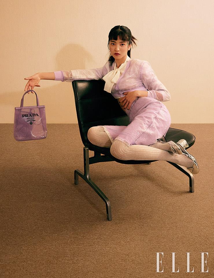 라벤더 크롭트 카디건과 스팽글 장식의 스커트, 리본 블라우스, 퍼플 크리놀린 토트백, 슬링백 슈즈, 스트라이프 스타킹은 모두 Prada.