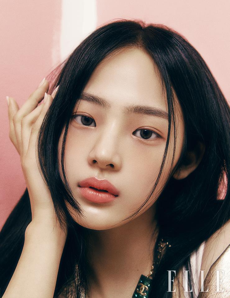 N°1 DE CHANEL 레드 까멜리아 파운데이션을 브러시로 얇게 펴 발라 화사하고 고르게 정돈된 민지의 피부. 양볼에서 시작해 눈 밑까지 N°1 DE CHANEL 레드 까멜리아 립 앤 치크 밤, 4 웨이크-업 핑크를 넓게 발라 순수하고 사랑스런 매력을 극대화한다. 싱그러운 라이트 핑크 톤의 바움 에쌍씨엘 글로우 스틱, 드라지를 이마와 콧등, 인중과 턱 끝에 레이어드해 차르르 빛나는 윤기를 더한 뒤, 입술에 건강하고 맑은 윤기를 표현하는 루쥬 코코 밤, 918 마이 로즈를 발라준다. 사용 제품은 모두 Chanel. 골드 점퍼와 네크리스는 모두 Chanel.