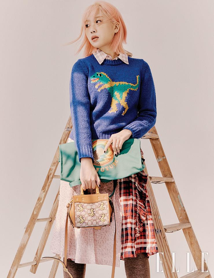 공룡 자수가 새겨진 렉시 스웨터와 레이어드한 체크 셔츠, 체크 패턴의 스커트와 에이프런 스커트, 오리 자수가 새겨진 시그너처 자카르 로그 백과 반으로 접어 든 리사이클 토트백, 레깅스는 모두 Coach.