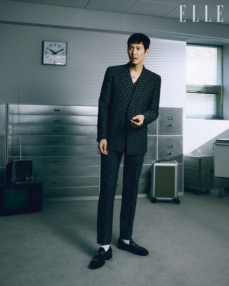 로고 패턴의 수트 재킷과 베스트, 팬츠, 펜던트 네크리스, 삭스, 홀스빗 로퍼, 트롤리는 모두 Gucci.