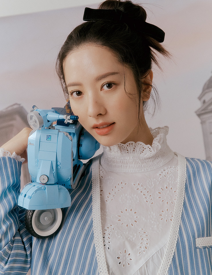 1960년대 클래식 베스파 피아지오 모델을 형상화한 파스텔 블루 컬러의 베스파 125는 LEGO. 스트라이프 패턴 재킷은 Romanchic. 화이트 러플 셔츠는 H&M. 리본 헤어 스트링은 Vintage Hollywood.