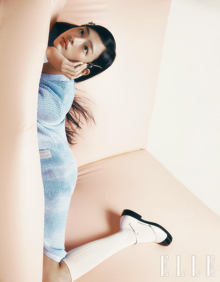 그저 가만히 있어도 숨겨지지 않는, 뉴 샤넬 걸 민지만의 독보적 매력! N°1 DE CHANEL 레드 까멜리아 파운데이션을 민지의 피부 결을 따라 얇게 펴 발라 화사하게 정돈한다. 수분감 가득한 리퀴드 블러셔인 레 베쥬 워터-프레시 블러셔, 라이트 피치를 양볼과 콧등까지 터치해 싱그러운 살굿빛 혈색을 표현해준 뒤, 루쥬 코코 밤, 916 플러티 코랄을 발라 비타민처럼 상큼한 톤 온 톤 코럴 메이크업을 완성한다. 사용 제품은 모두 Chanel. 하늘색 롱 카디건과 메리 제인 슈즈, 헤어핀과 네크리스는 모두 Chanel. 이너 웨어로 입은 화이트 톱과 니 삭스는 모두 스타일리스트 소장품