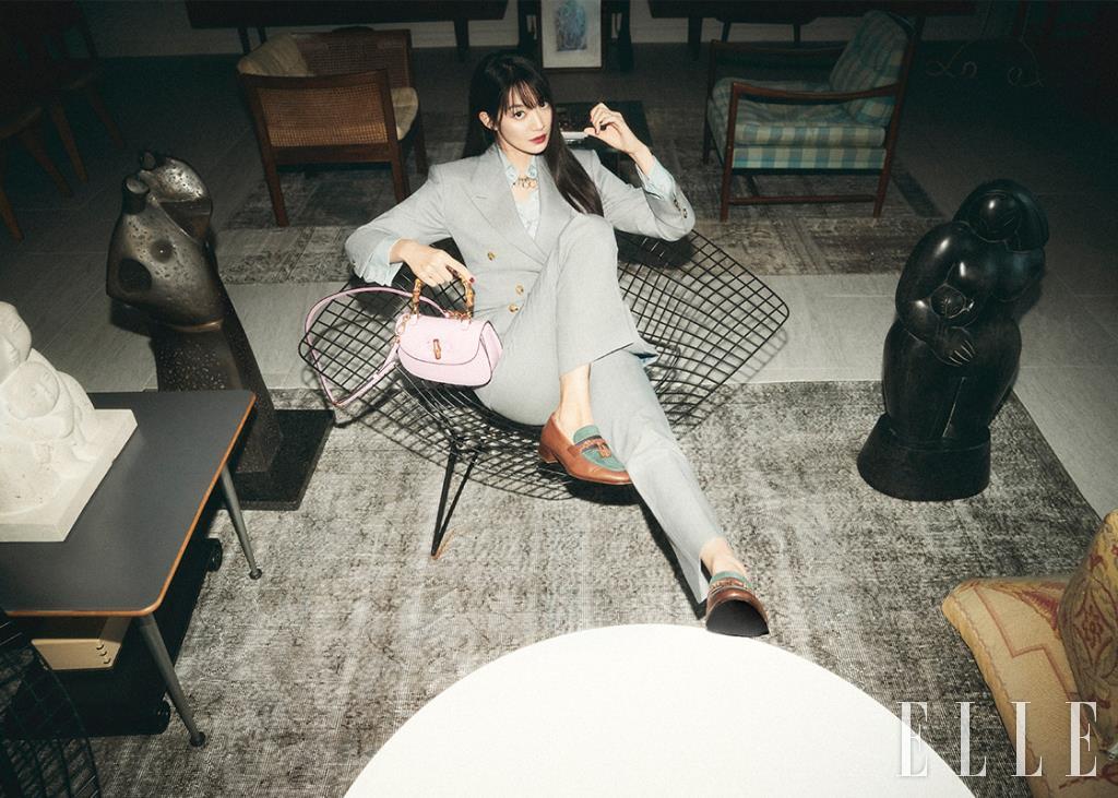 그레이 더블 브레스티드 울 재킷과 팬츠, 라이트 블루 셔츠, 로고 포인트 네크리스, 뱀부 톱 핸들이 돋보이는 핑크 스몰 톱 핸들 백, 태슬 장식의 로퍼는 모두 Gucci.