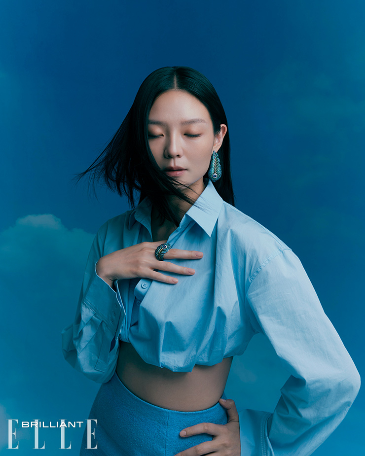 2개의 오벌 탄자나이트, 31개의 사파이어, 240개의 차보라이트, 58개의 브라운 다이아몬드를 장식한 화이트 골드와 티타늄 소재의 ‘탄자나이트 플륌 드 펑’ 이어링은 7천만원대, 1개의 오벌 탄자나이트, 123개의 사파이어, 85개의 차보라이트, 43개의 브라운 다이아몬드, 19개의 화이트 다이아몬드를 장식한 화이트 골드와 티타늄 소재의 ‘탄자나이트 플륌 드 펑 라지’ 링은 3천만원대 모두 BOUCHERON. 크롭트 셔츠는 Jacquemus. 미니스커트는 PATOU.