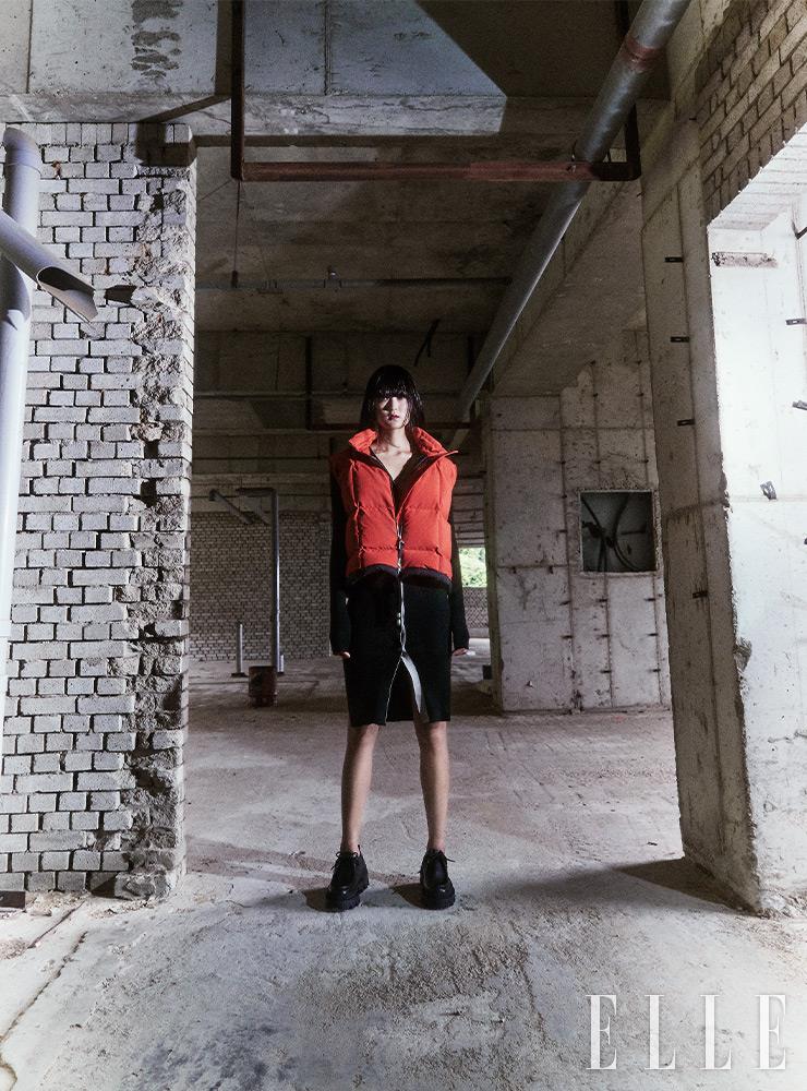 경쾌한 오렌지 컬러의 슬리브리스 패딩 아우터웨어와 버튼다운 니트 드레스는 모두 2 Moncler 1952. 레이스업 슈즈는 Moncler Collection. 