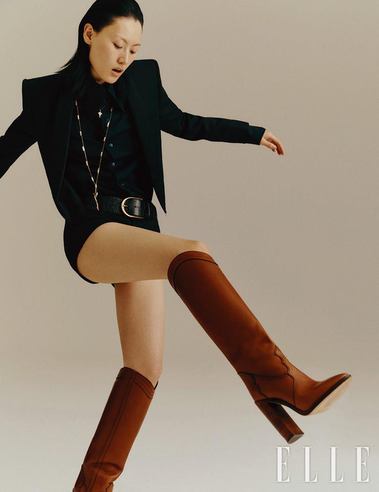  레이어드한 두 개의 네크리스, 날렵한 셰이프의 크롭트 재킷, 블랙 셔츠, 빅 버클 와이드 벨트, 마이크로 쇼츠와 웨스턴 스타일의 부츠는 가격 미정, 모두 Saint Laurent by Anthony Vaccarello. 