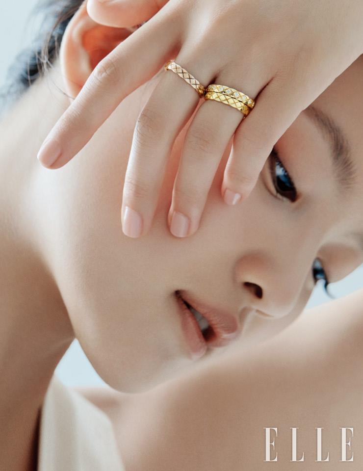 약지에 레이어드한 옐로골드 코코 크러쉬 미니 링과 다이아몬드 세팅의 옐로골드 코코 크러쉬 미니 링, 중지의 베이지골드 코코 크러쉬 미니 링은 모두 Chanel Fine Jewelry. 